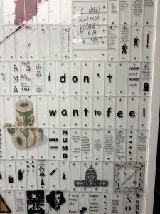 I Don't Want to Feel - Under the Microscope Part of an art installation, this image displays a wall covered in white panels with various texts and images related to addiction, recovery, and emotional distress. Central to the composition is the large, bold text 'i don't want to feel' with each letter on a separate panel. Surrounding this are phrases like 'NUMB DUMB,' 'I NEED Treatment PLEASE!!,' and 'On off On off 302 Go to Rehab AMA.' There are also references to Hepatitis C, emotional states, and a piece of text resembling a crossword puzzle with the words 'DRUG COURT EDITION.' Images include the Capitol building, pills, and a tear-stained face, creating a compelling collage that speaks to the complexity of substance abuse and the struggle for recovery. Under the Microscope immersive sculpture by Maria Maneos